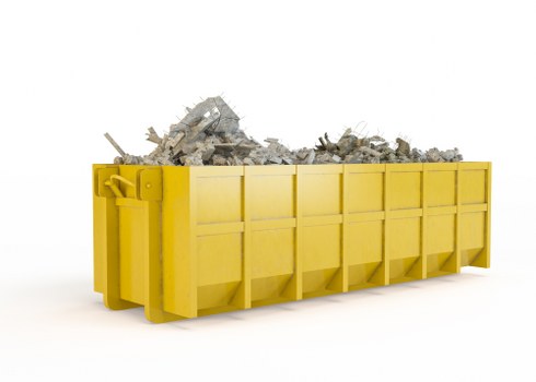 A large, rectangular skip with a bright yellow exterior, situated outdoors against a plain white background. The skip is filled with a substantial amount of mixed construction debris, including broken concrete slabs, bricks, and other rubble, which are piled up above the top edges of the container. The debris displays various shades of grey and tan, with some rough textures and jagged edges visible. The skip's sturdy metal sides feature vertical and horizontal reinforcements, and the environment suggests a commercial or industrial setting, typical of waste removal operations in Cheshunt. The skip is positioned on a flat, even surface, which could be a driveway or paved area, and the scene captures a straightforward, detailed view of the waste materials ready for collection by Commercial Waste Cheshunt as part of their rubbish clearance services.